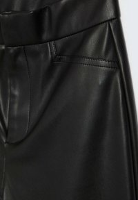 Detailní záběr na černé kalhoty z imitace kůže, zobrazující pásek, detaily kapes a hladký texturovaný povrch se šitými švy.