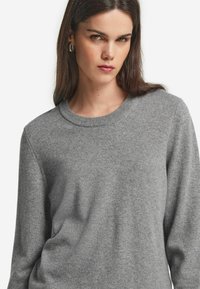 Grau gestrickter Pullover aus weichem Material, mit klassischem Rundhalsausschnitt und langen Ärmeln, im lässigen Schnitt und mit subtiler Textur.