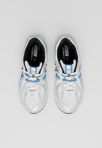 Vita atletiska skor med blå accenter, meshovandel för andningsförmåga, texturerad sula för grepp och traditionellt snörsystem.