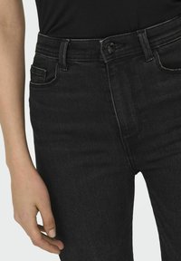 Jeans de mezclilla negros que presentan un diseño ajustado, estilo de cinco bolsillos y un cierre con botón en la cintura. La textura parece suave con un ligero estiramiento.