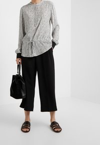 Blouse à manches longues avec une base blanche et un motif floral noir, associée à un pantalon large noir et des sandales noires glissantes.