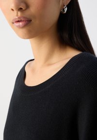 Black knitted sweater with a wide neckline, showcasing a textured pattern. Silver hoop earring visible on the right ear.