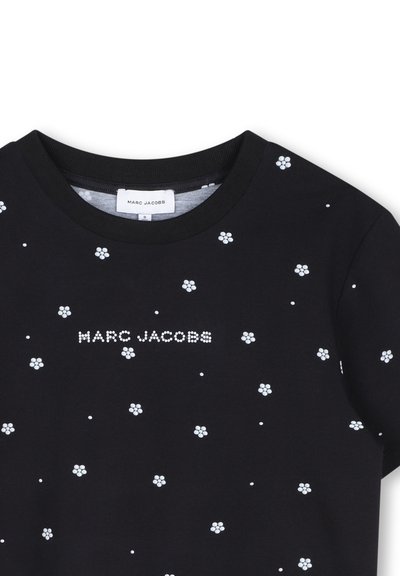 Μαύρο t-shirt Marc Jacobs με λευκά πουά λουλουδένια σχέδια και το όνομα της μάρκας «Marc Jacobs» σε λευκές κουκκίδες στο στήθος.
