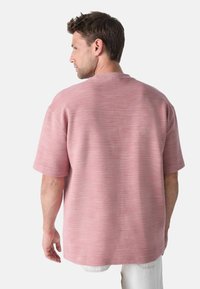 Camisa de manga corta en color rojo ladrillo, con un patrón texturizado a rayas y un diseño de corte relajado, con cuello redondo.