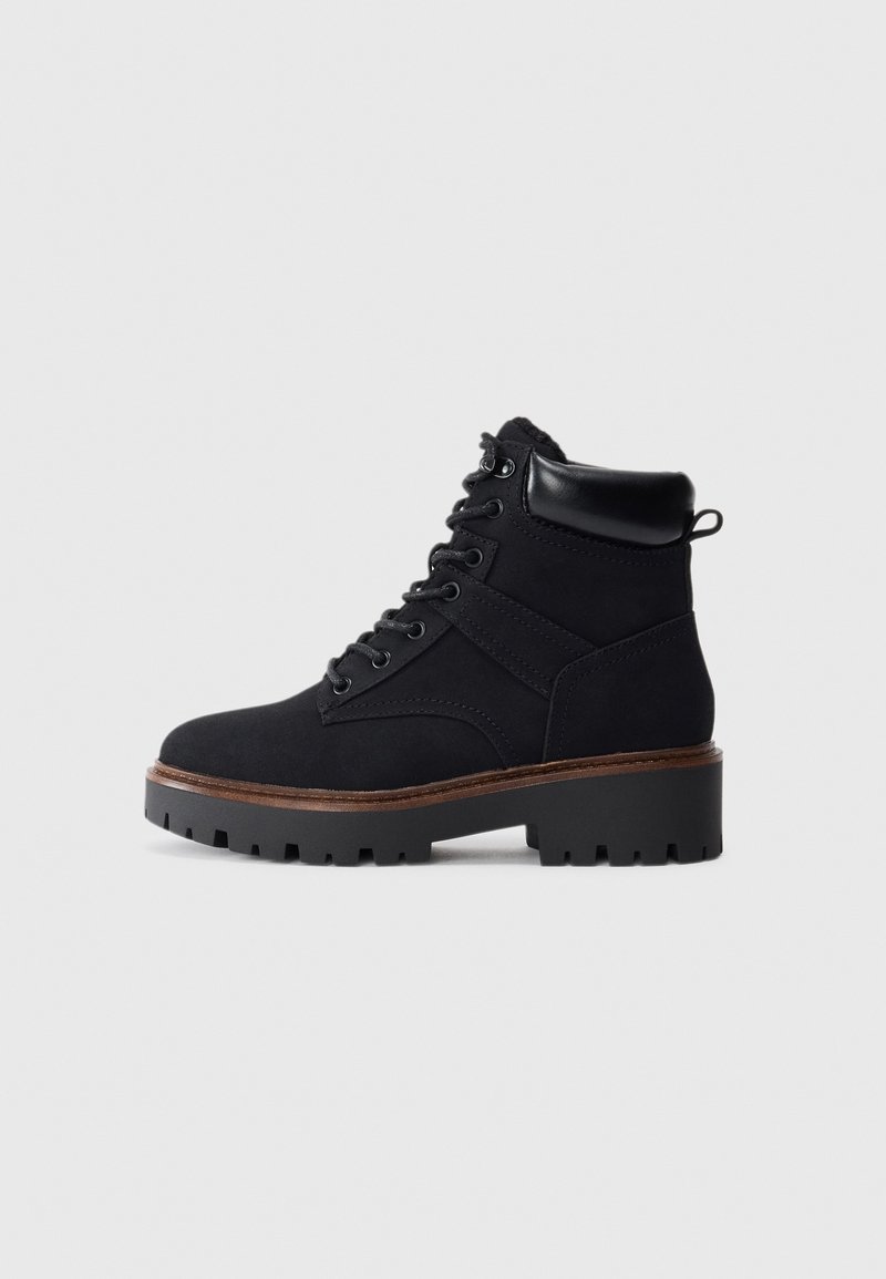 Bottine noire à lacets avec col rembourré, semelle à crampons épaisses et détail de bordure marron, vue de profil.