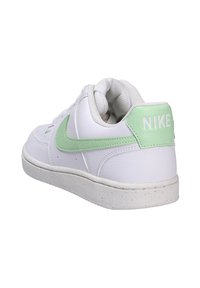 Zapatilla blanca de cuero con acentos verdes, que cuenta con un collar acolchado y una lengüeta texturizada, diseño ligero y suela de goma salpicada.