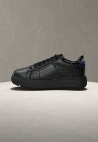 Μαύρο sneaker χαμηλού ύψους με διάτρητα σε σχήμα καρδιάς, λογότυπο "LOVE MOSCHINO" και γυαλιστερή λεπτομέρεια στη φτέρνα σε σκούρο μπλε χρώμα πάνω σε ουδέτερο υπόβαθρο.