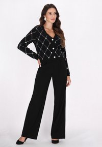 Cardigan nero in maglia con un motivo a diamante, caratterizzato da abbellimenti colorati e un scollo a V, abbinato a pantaloni neri a vita alta.
