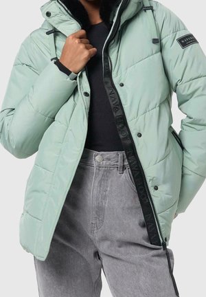 Person wearing a mint green puffer jacket with black fleece lining and gray jeans, hand adjusting the jacket collar.
