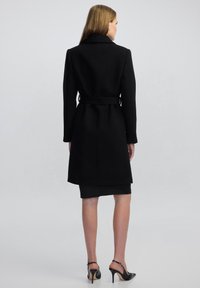 Cappotto in lana nera con cintura. Caratterizzato da un colletto a punta, maniche lunghe e una vestibilità sagomata. Design fino al ginocchio con una texture liscia.