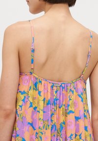 Floral dress featuring pastel colors, thin straps, and a pleated texture. The back is semi-open with an attached brand tag near the seam.