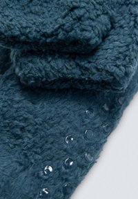 Manta de forro polar en verde azulado oscuro, con una superficie texturizada y puntos elevados a lo largo de un borde para un mejor agarre. Material suave y acolchado.