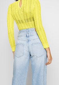 Gul långärmad topp med ribbad textur och glänsande detaljer, tillsammans med högmidjade ljusblå vida jeans med bakfickor.