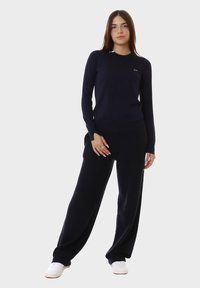 Completo da loungewear in maglia blu navy, composto da una maglietta a maniche lunghe con scollo rotondo e pantaloni dalla vestibilità rilassata, abbinato a sneakers bianche per un contrasto.