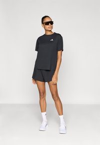 Tmavomodré športové tričko s krátkymi rukávmi, doplnené o zodpovedajúce krátke nohavice. Obsahuje jemný detail loga a štýlové okuliare na športové použitie.