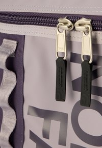 Γκρι και μωβ σακίδιο πλάτης με φερμουάρ YKK, με υφασμάτινη υφή και έντονο τυπωμένο λογότυπο, με μαύρους λαστιχένιους τράβηγμα φερμουάρ ως τόνους.