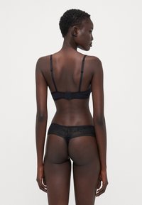 Ensemble de soutien-gorge noir et de string en dentelle. Le soutien-gorge présente des bretelles fines et un fermoir sécurisé au dos. Le string a des accents en dentelle florale et une texture transparente.