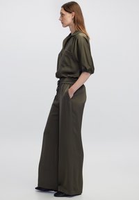 Olijfgroene satijnen outfit met een gekraagde short-sleeve blouse met een borstzak en wijde broek met een elastische tailleband.