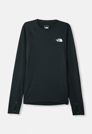 Chemise noire à manches longues en tissu texturé, avec un col rond et des fentes sur les manches. Le logo de la marque est affiché de manière proéminente.