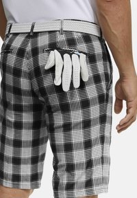 Schwarz-weiße Karotten-Shorts mit einem geflochtenen weißen Gürtel, in der rechten hinteren Tasche ist teilweise ein weißer Golfhandschuh versteckt.