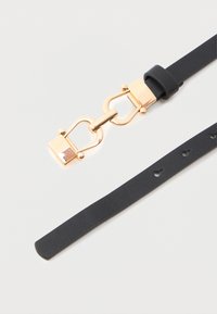 Fekete bőr öv arany színű fém csattal és több állítólyukkal fehér háttér előtt.
