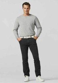 Grijze sweatshirt, zwarte jeans en witte sneakers. De riem is geweven wit met zwarte accenten. De pasvorm is casual en gestroomlijnd.