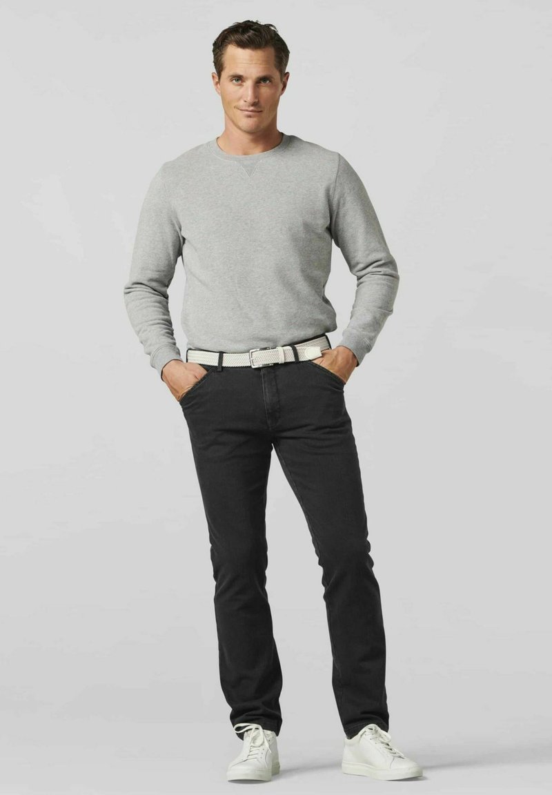 Grijze sweatshirt, zwarte jeans en witte sneakers. De riem is geweven wit met zwarte accenten. De pasvorm is casual en gestroomlijnd.