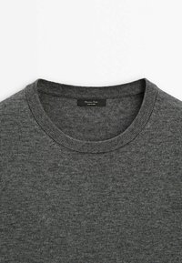 Pull en tricot gris foncé à col rond avec col côtelé et une étiquette noire cousue à l'intérieur de l'encolure.