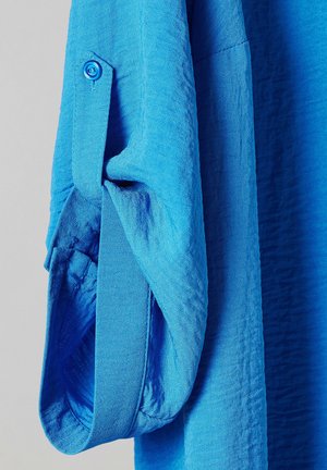 Felle blauwe shirtstof met een gestructureerde afwerking. Kenmerkt zich door een knoopmanchet en opgerolde mouwen. Gladde oppervlakte met subtiel weefpatroon.