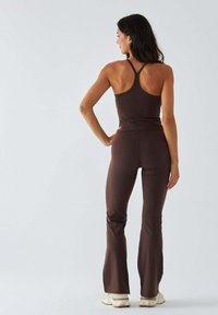 Czekoladowobrązowy zestaw sportowy składający się z topu na ramiączkach typu racerback i rozszerzanych legginsów, wykonany z gładkiej, elastycznej tkaniny zapewniającej komfort i elastyczność.