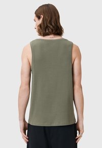 Olivgrünes ärmelloses Tanktop mit rundem Ausschnitt, geripptem Saum und glatter Oberfläche, getragen mit schwarzen Hosen.