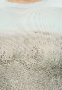 Κοντινό πλάνο ενός ανοιχτόχρωμου πλεκτού πουλόβερ με χνουδωτές, υφασμάτινες ίνες και φαρδύ λαιμόκοψη σε ένα άτομο.