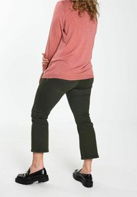 Maglietta a maniche lunghe rosa chiaro abbinata a pantaloni neri a sigaretta verdi scuri e mocassini neri spessi. Il tessuto appare morbido con una vestibilità rilassata.