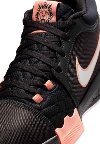 Black athletic shoe featuring a textured upper, pink accents, and a prominent white logo. Lace-up design with a padded collar.