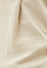 Beige linnetyg med en texturerad yta, som visar fina vävda mönster och mjuk häng. Lätt, andningsbar material som passar för kläder.