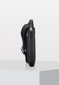 Borsa a tracolla nera con superficie testurizzata, profilo sottile, tracolla regolabile e accessori in metallo argentato, dotata di chiusura con zip superiore.