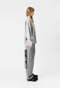 Sudadera gris con hombros caídos, pantalones de chándal grises a juego que cuentan con una etiqueta lateral, y zuecos negros texturizados. Diseño simple y funcional.