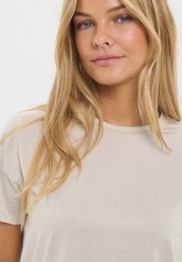 Light beige, short-sleeve shirt featuring a soft, shimmery texture. Round neckline and relaxed fit, with subtle sheen across the fabric.