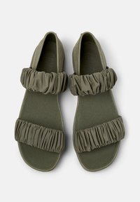Sandali verde oliva realizzati in tessuto morbido con cinturini arricciati, dotati di suola piatta e design con punta aperta. Stile testurizzato e minimalista.