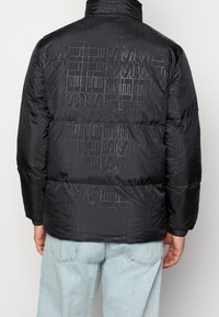 Czarna pikowana kurtka z wysokim kołnierzem, posiadająca błyszczący, fakturowany wzór. Materiał jest gładki i pikowany, o luźnym kroju.