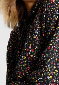 Felpa nera con cappuccio caratterizzata da un motivo floreale con piccoli fiori colorati in rosso, giallo, bianco e viola; tessuto strutturato con una vestibilità ampia.