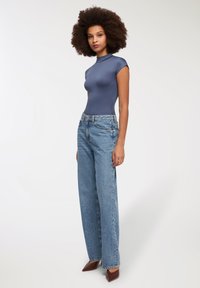 Dopasowany granatowy body z wysokim dekoltem, w połączeniu z szerokimi, jasnoniebieskimi dżinsami i brązowymi szpilkami w szpic, na neutralnym tle.