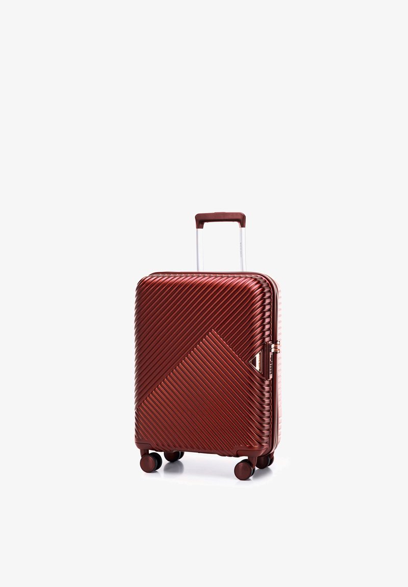 Valise rigide rouge avec texture en diagonale rainurée, quatre roues et poignée argentée déployée sur fond blanc.