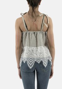 Canotta di cotone a righe con pizzo lungo l'orlo, dotata di spalline regolabili e un design leggero, indossata con jeans blu.