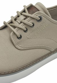 Beež kangast sneaker valge kummist tallaga, millel on metallist silmad, pruun nahkdetail ja reljeefne logo külgedel.