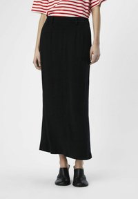 Jupe noire longueur cheville avec une texture lisse, dotée d'une taille cintrée et de plis subtils. Portée avec un haut rayé rouge et blanc.