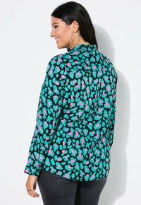Mehrfarbige Bluse mit einem türkisfarbenen, pinken und schwarzen abstrakten Leopardenmuster; lange Ärmel mit Manschette, Knopfverschluss und Rückenpasse.