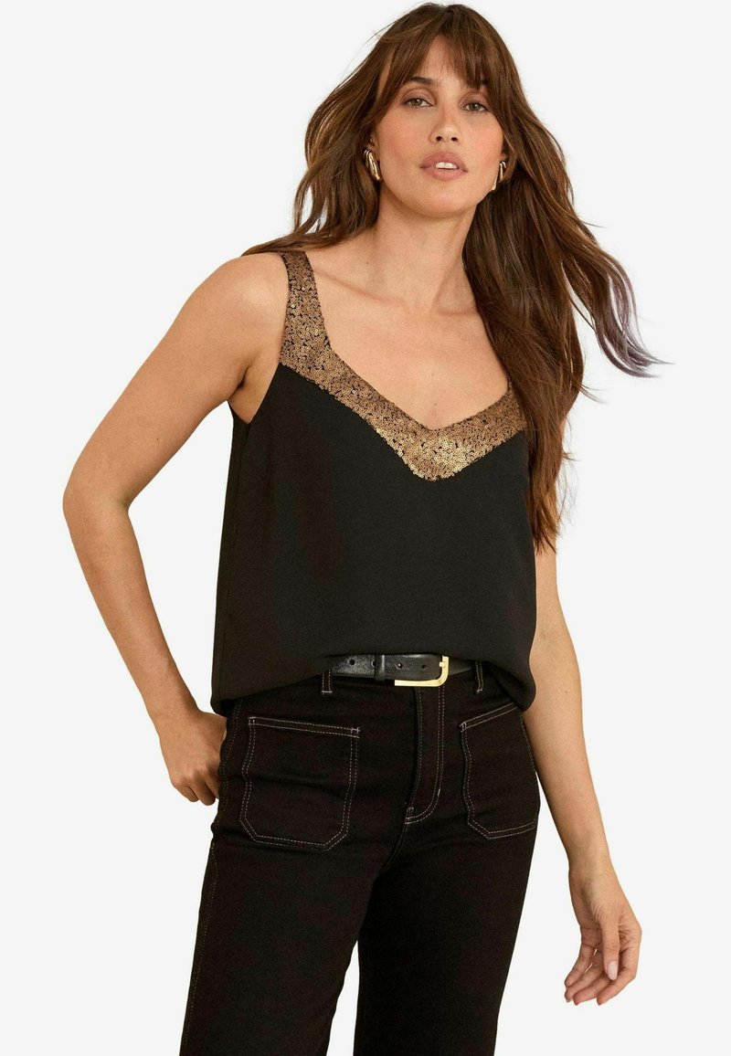 Top nero senza maniche con scollo a V, decorato con un bordo in pizzo dorato lungo l'escollatura, abbinato a jeans neri e a una cintura nera.
