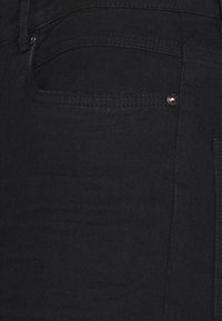 Jeans de mezclilla negra con un diseño clásico de cinco bolsillos, que presentan una textura sutil y detalles en metal dorado en el bolsillo delantero.