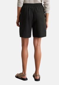 Schwarze Baumwollshorts mit einem elastischen Bund, geradem Bein und einer einzigen Gesäßtasche, kombiniert mit braunen Schuhen.
